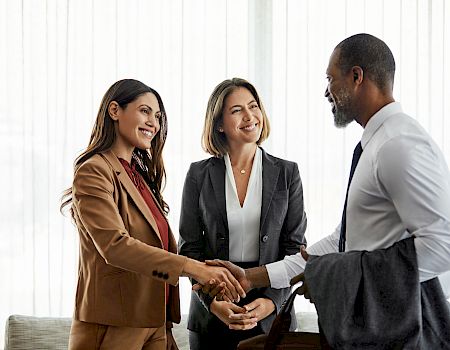 Three people in business attire are talking and shaking hands, suggesting a professional or business meeting setting.