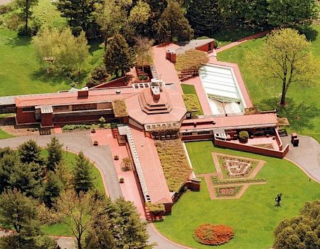 An aerial view of a large, architecturally unique building surrounded by lush greenery and landscaping.